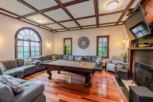 Cozy living room with a pool table, gray sofas, wooden ceiling, and large windows letting in natural light.