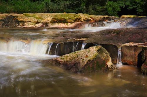 A serene waterfall cascading over rocky ledges into a calm river, surrounded by lush greenery.