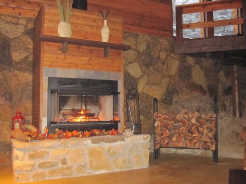 Cozy living room with a stone fireplace, wooden accents, and autumn leaves decor. Warm and inviting atmosphere.