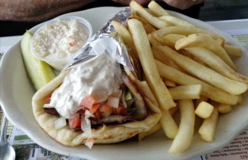 A plate featuring a wrapped gyro with sauce, lettuce, and tomatoes, served with fries and a side of coleslaw.