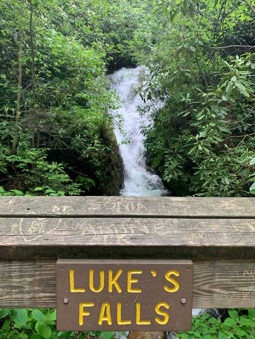 A wooden sign reading "Luke's Falls" overlooks a cascading waterfall surrounded by lush greenery.