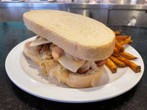 A sandwich with layers of meat, cheese, and sauerkraut, served with a side of sweet potato fries on a white plate.