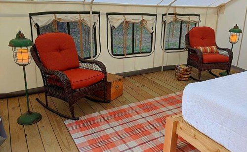 Cozy tent interior with two red rocking chairs, a plaid rug, and warm lighting, creating a welcoming atmosphere.