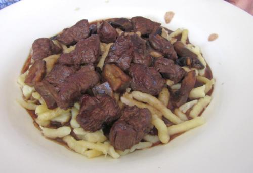 A plate of tender beef chunks served over a bed of pasta with mushrooms in a rich sauce.