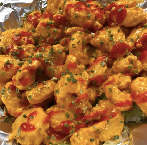 A close-up of crispy chicken pieces coated in orange cheese sauce, drizzled with ketchup and topped with green onions.