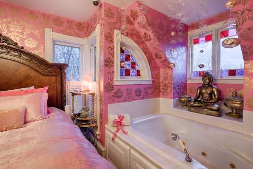 A vibrant pink bathroom with a large tub, decorative Buddha statue, and elegant wallpaper featuring gold patterns.