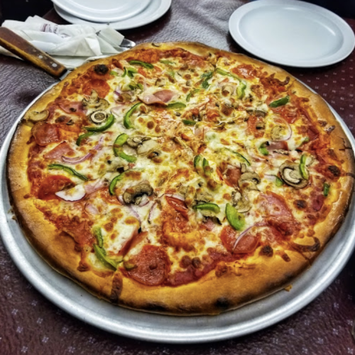 A large pizza topped with pepperoni, ham, mushrooms, green peppers, and cheese on a silver platter.