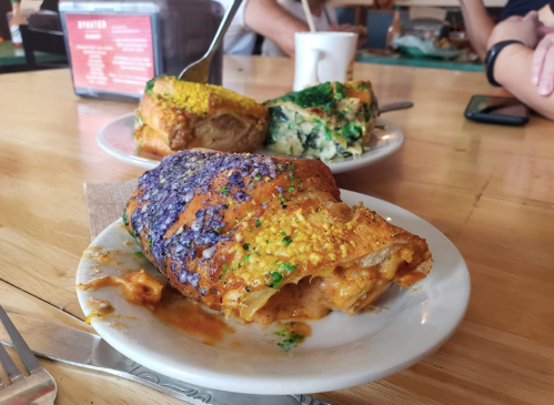 Two colorful pieces of king cake on white plates, with vibrant icing and sprinkles, on a wooden table.