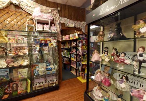 A colorful toy store interior featuring glass display cases filled with dolls, toys, and children's books.