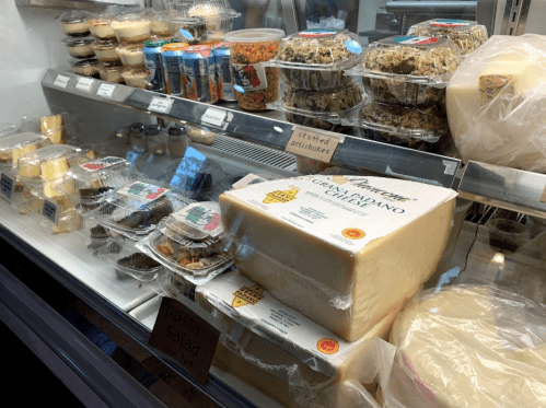 A display case filled with various food items, including cheese, salads, desserts, and drinks.