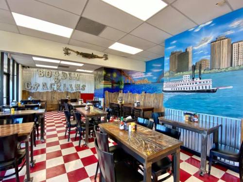 Interior of a restaurant with checkered floors, wooden tables, and a colorful mural depicting a waterfront scene.
