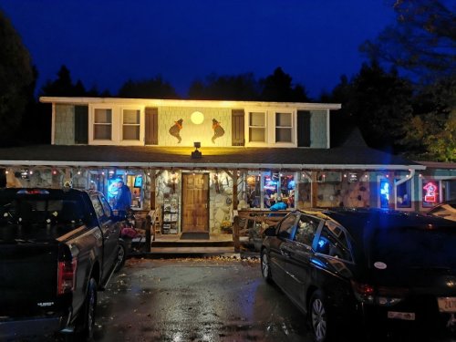 A cozy, illuminated restaurant with stone exterior and festive lights, surrounded by parked cars at dusk.