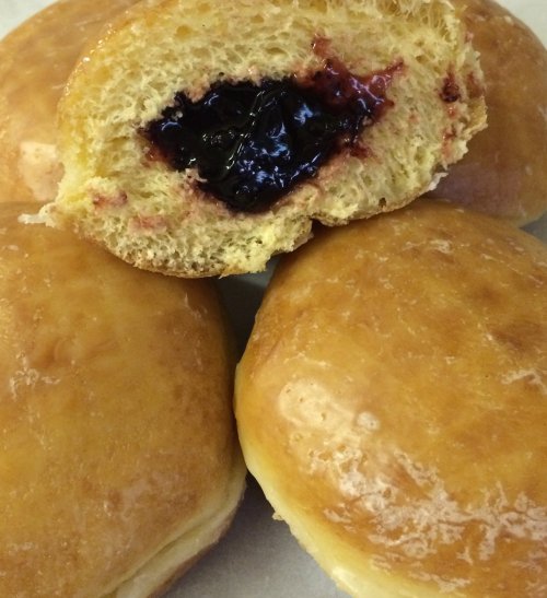 A close-up of a glazed donut with a bite taken out, revealing a rich berry filling, surrounded by whole donuts.