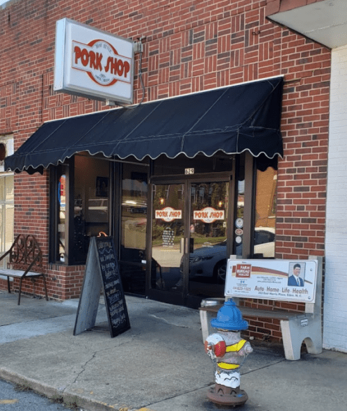 Exterior of a brick building featuring a sign that reads "Pork Shop," with a fire hydrant and sidewalk in front.