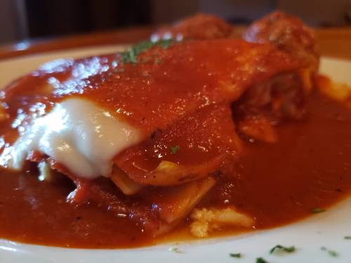 A close-up of a plate of lasagna topped with marinara sauce and melted cheese, garnished with parsley.