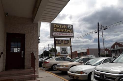 Sign for Dutch Country Restaurant with cloudy skies and parked cars in front.