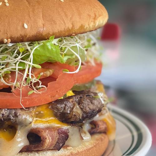 A close-up of a delicious burger with layers of cheese, lettuce, tomato, sprouts, and pickles on a sesame seed bun.