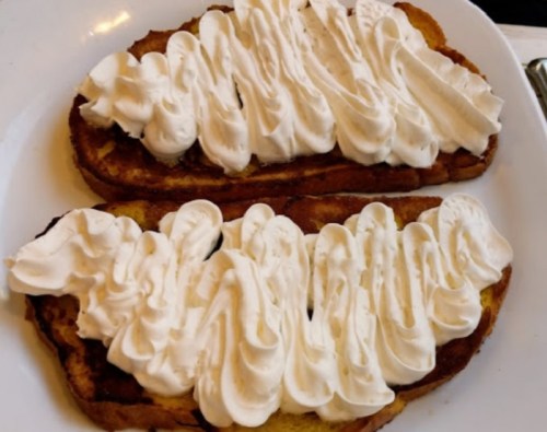 Two slices of French toast topped with a generous swirl of whipped cream on a white plate.