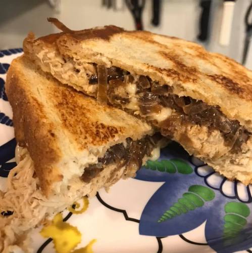 Close-up of a toasted sandwich filled with shredded meat and melted cheese, served on a decorative plate.