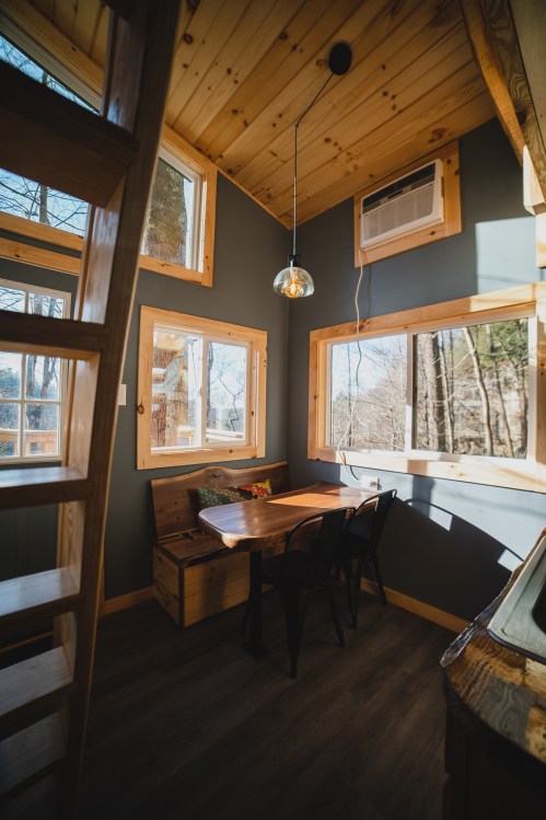 Cozy interior of a tiny house featuring a wooden table, chairs, and large windows with natural light.