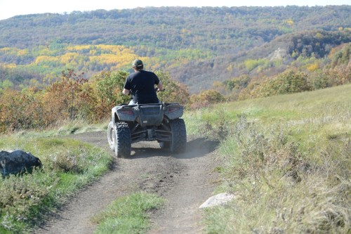 A person riding an ATV on a dirt path, surrounded by colorful autumn foliage and rolling hills.