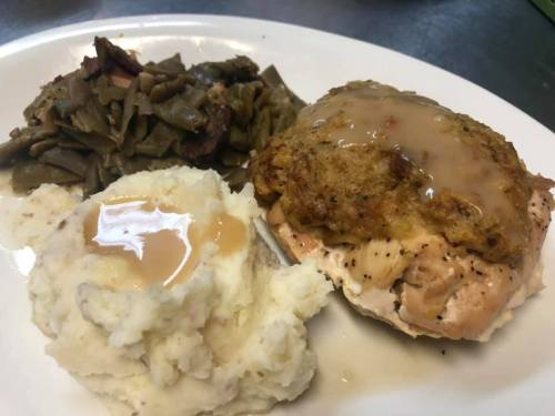 A plate of food featuring baked chicken with stuffing, green beans, and mashed potatoes topped with gravy.