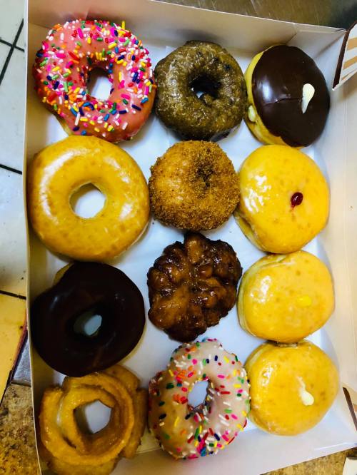 A box of assorted donuts, featuring glazed, chocolate, and sprinkled varieties, arranged in two rows.