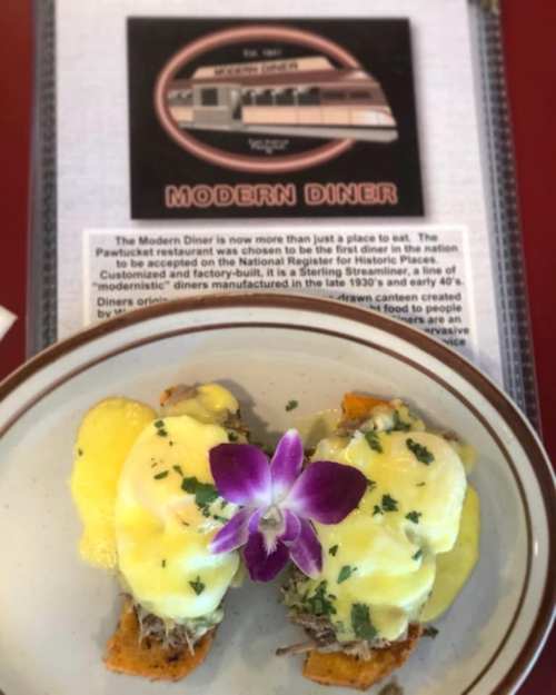 A plate of eggs benedict with a flower garnish, served at the Modern Diner, featuring a vintage diner menu in the background.