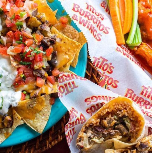 A colorful plate of nachos topped with cheese, salsa, and a side of wings and veggies, served in a basket.