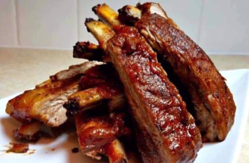 A plate of succulent, glazed barbecue ribs stacked on a white dish, showcasing a rich, caramelized sauce.