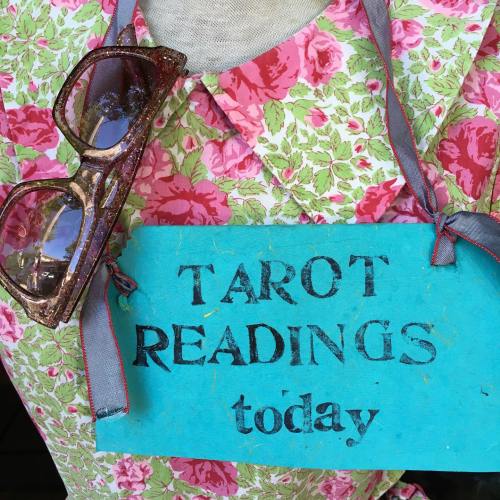 A floral dress with sunglasses and a blue sign that reads "TAROT READINGS today."