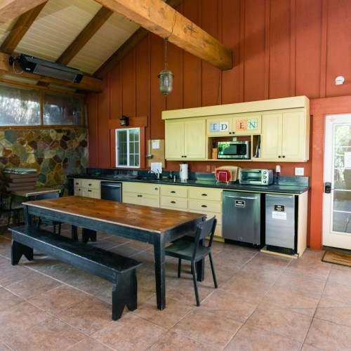 A rustic kitchen with wooden beams, a large table, and modern appliances against a red wall.