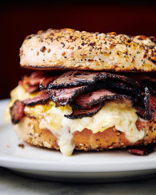 A close-up of a toasted bagel sandwich filled with melted cheese and layers of sliced roast beef.