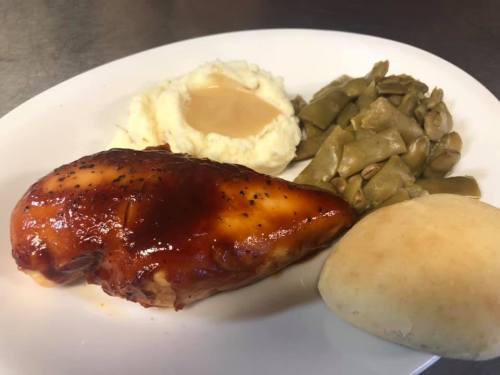 A plate featuring barbecue chicken, mashed potatoes with gravy, green beans, and a dinner roll.