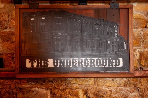 A metal sign depicting a historic building with the text "The Underground" on a rustic stone wall.