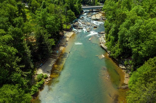 Aerial view of a river winding through lush greenery, with rocks and a small bridge in the background.