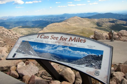 Sign at a mountain viewpoint titled "I Can See for Miles," featuring a panoramic landscape and distant mountain ranges.