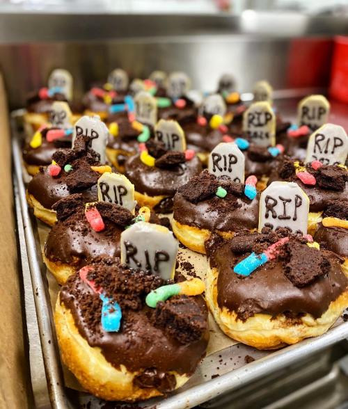 A tray of chocolate-covered donuts decorated with tombstone-shaped candies and colorful gummy worms.