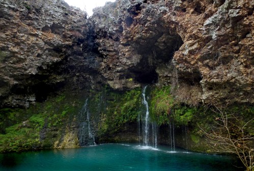 A serene natural scene featuring a rocky cave with two waterfalls cascading into a turquoise pool below.