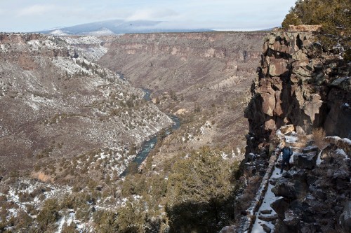 A scenic view of a snowy canyon with a river winding through, surrounded by rocky cliffs and sparse trees.