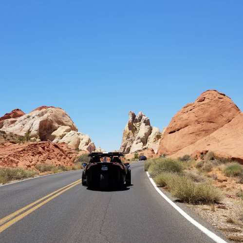 A car drives on a winding road surrounded by colorful rock formations under a clear blue sky.