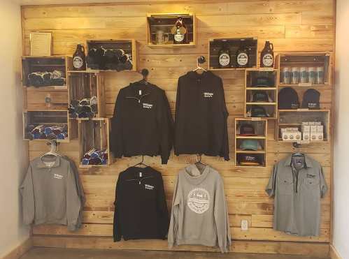 Merchandise display featuring hoodies, shirts, hats, and accessories on a wooden wall with shelves.