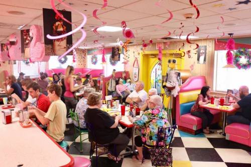A vibrant diner scene with colorful decor, patrons enjoying meals at booths and tables, and festive decorations hanging.