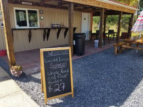 A wooden sign outside a food stand advertising a Wednesday special: whole rack and four sides for $27.