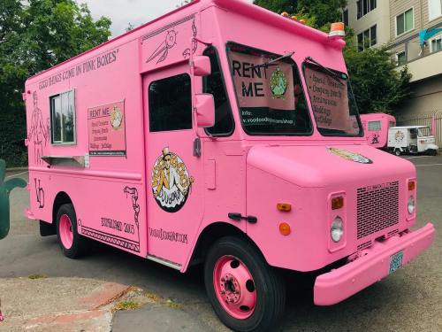 A bright pink food truck with various logos and text, parked on a street, offering rental information.