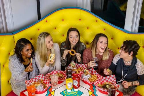 A group of five friends enjoying a meal together at a colorful diner, laughing and sharing food.