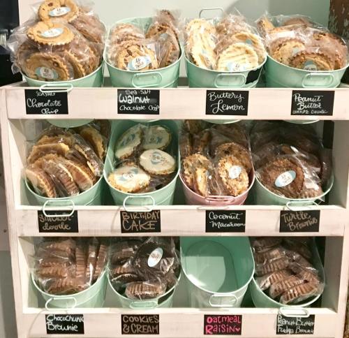 A display of assorted cookies in green buckets, labeled with flavors like chocolate chip, lemon, and birthday cake.