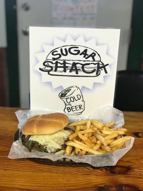 A burger with cheese and pickles served with fries, next to a sign that reads "Sugar Shack" and "Cold Beer."