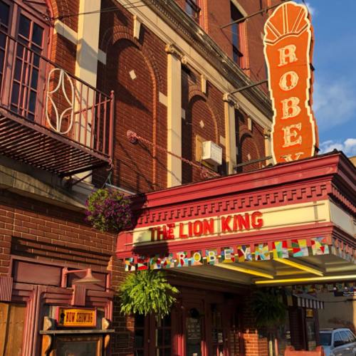 The Robey Theater marquee displays "The Lion King," with colorful flags and greenery adorning the entrance.