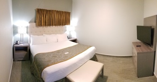 Cozy hotel room featuring a queen bed, bedside lamps, a TV, and a modern decor with a neutral color palette.